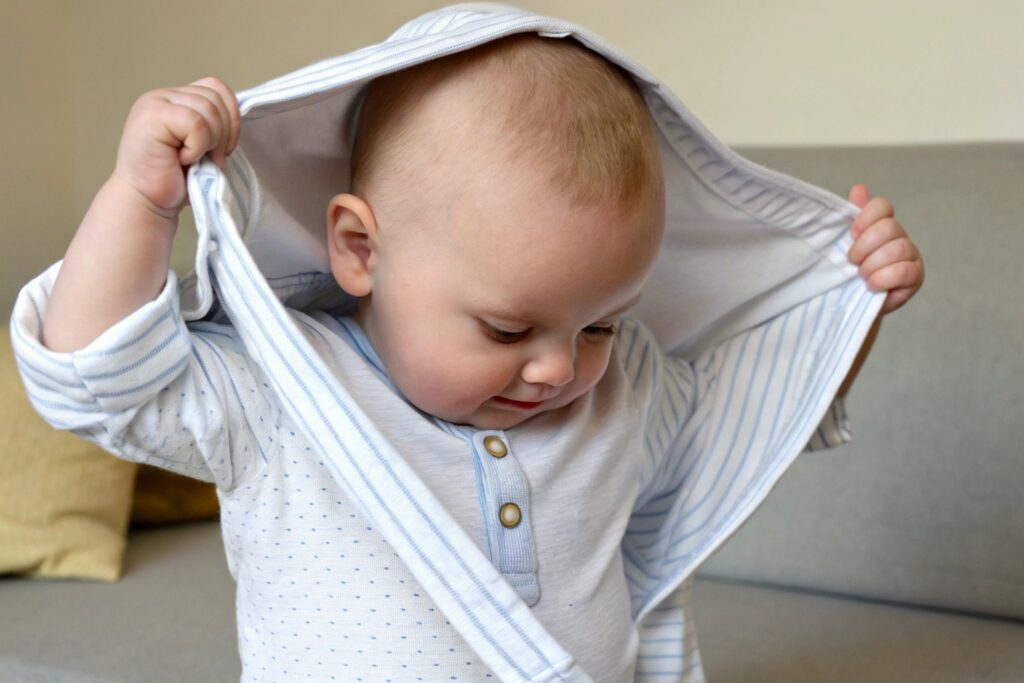 Child happily putting on a striped baby shirt, showing ease and comfort