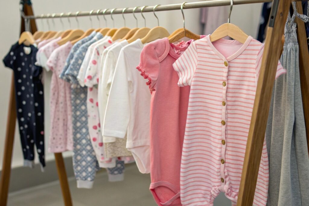 Clothing rack with a variety of girls' clothes, including pink and striped onesies