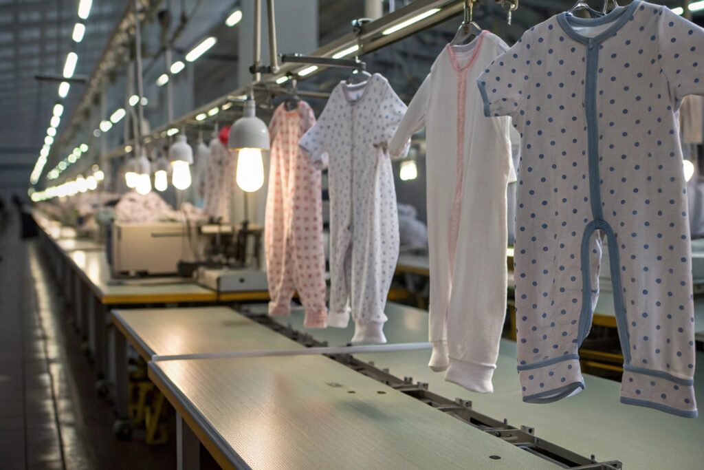 Baby clothing items hanging in a factory with sewing machines in the background
