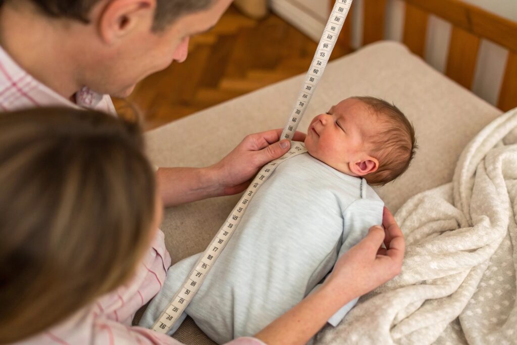 parents measuring newborn baby with tape measure for sizing