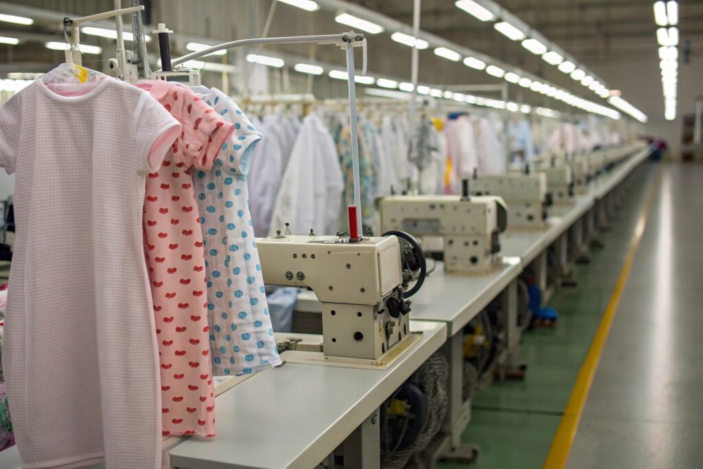 Row of industrial sewing machines with baby clothes on hangers, ready for production