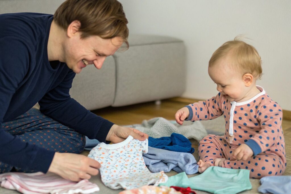 European Parent Watching Their Child Playing with Baby Clothes