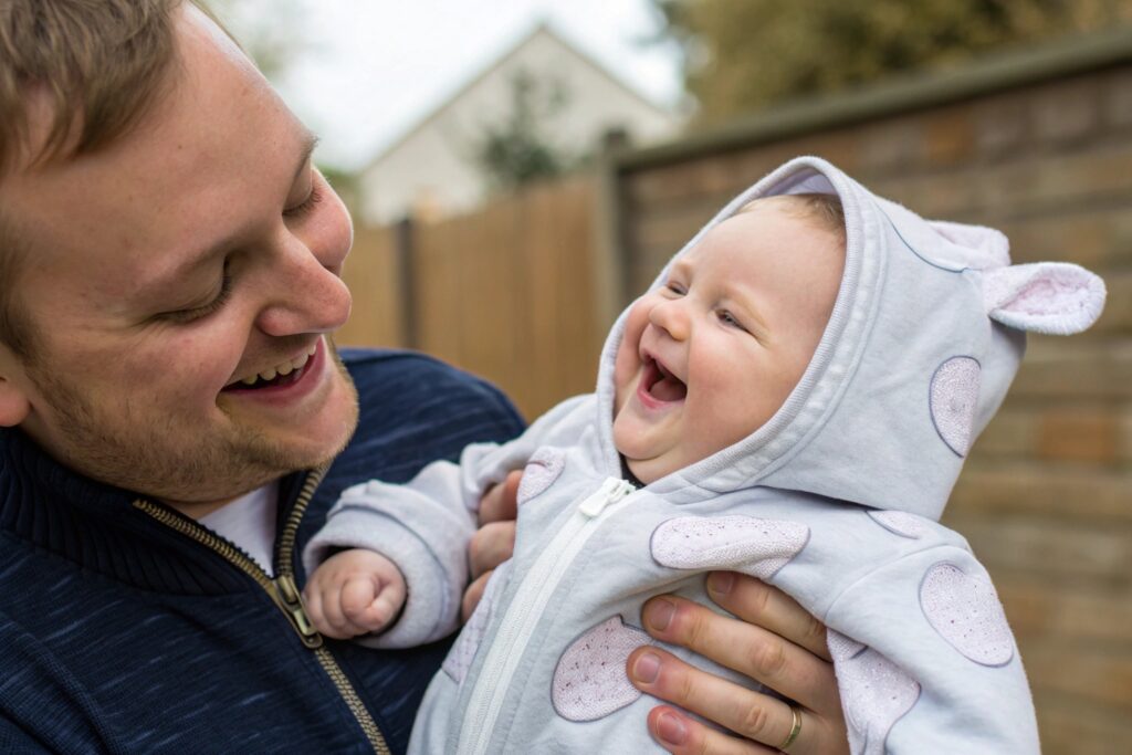 Parent smiling while holding a laughing baby in a cute hoodie