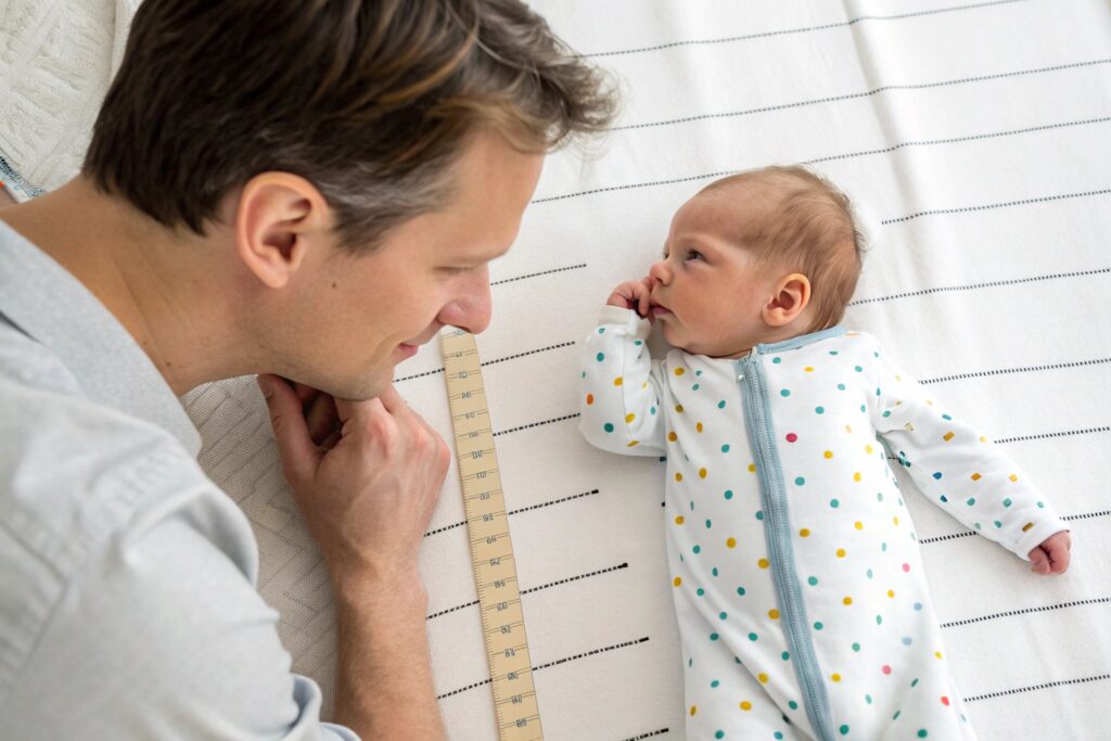 Newborn baby in colorful onesie with father, baby size comparison