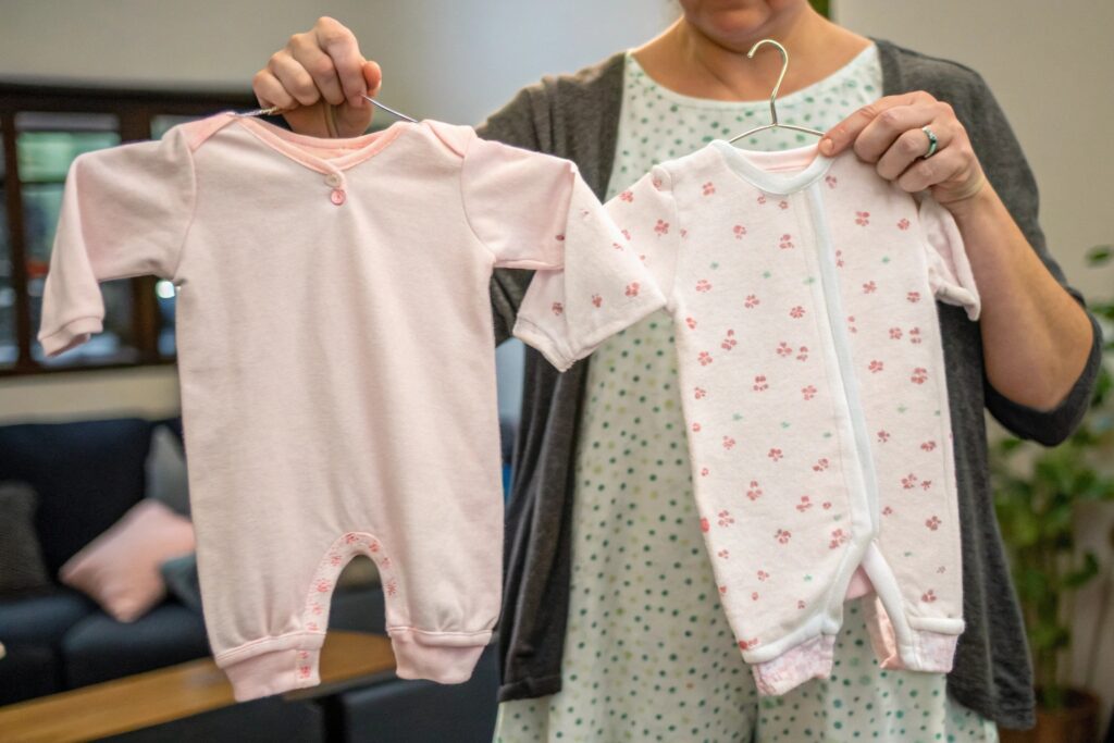 Parent holding up two baby outfits for comparison Parent holding up two baby outfits