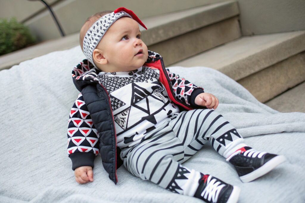 Stylish baby wearing a patterned hoodie, geometric print outfit, and sneakers outdoors