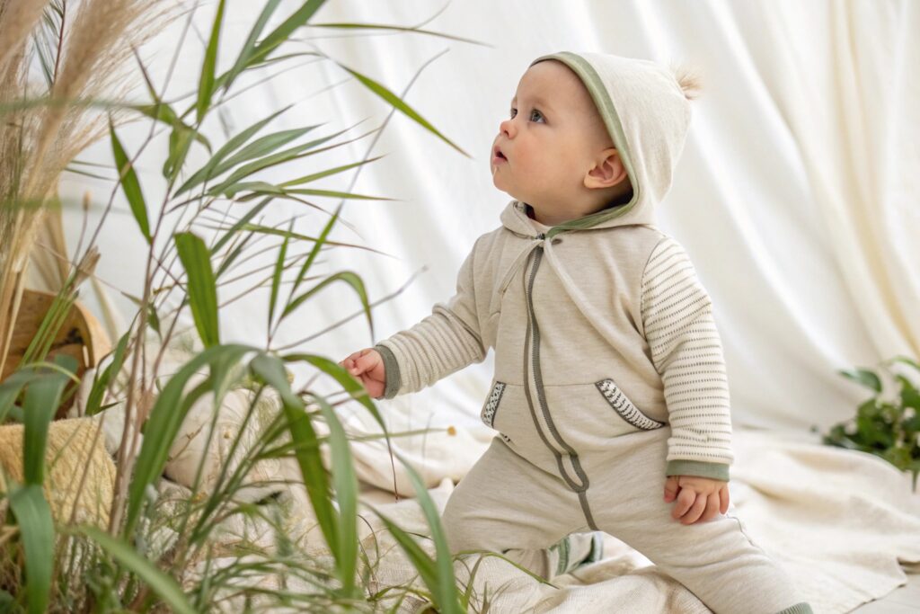 Curious baby in a soft, hooded onesie exploring plants in a serene environment