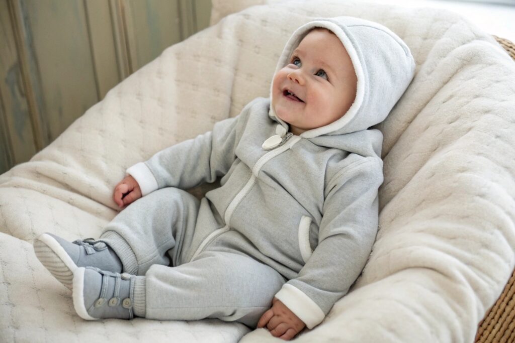 Smiling baby wearing a soft gray hoodie and matching pants, sitting comfortably on a cozy chair