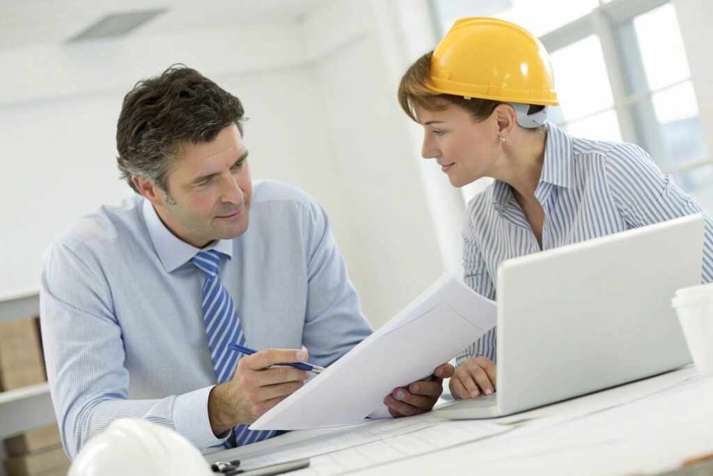 Two professionals discussing blueprints and plans in an office setting